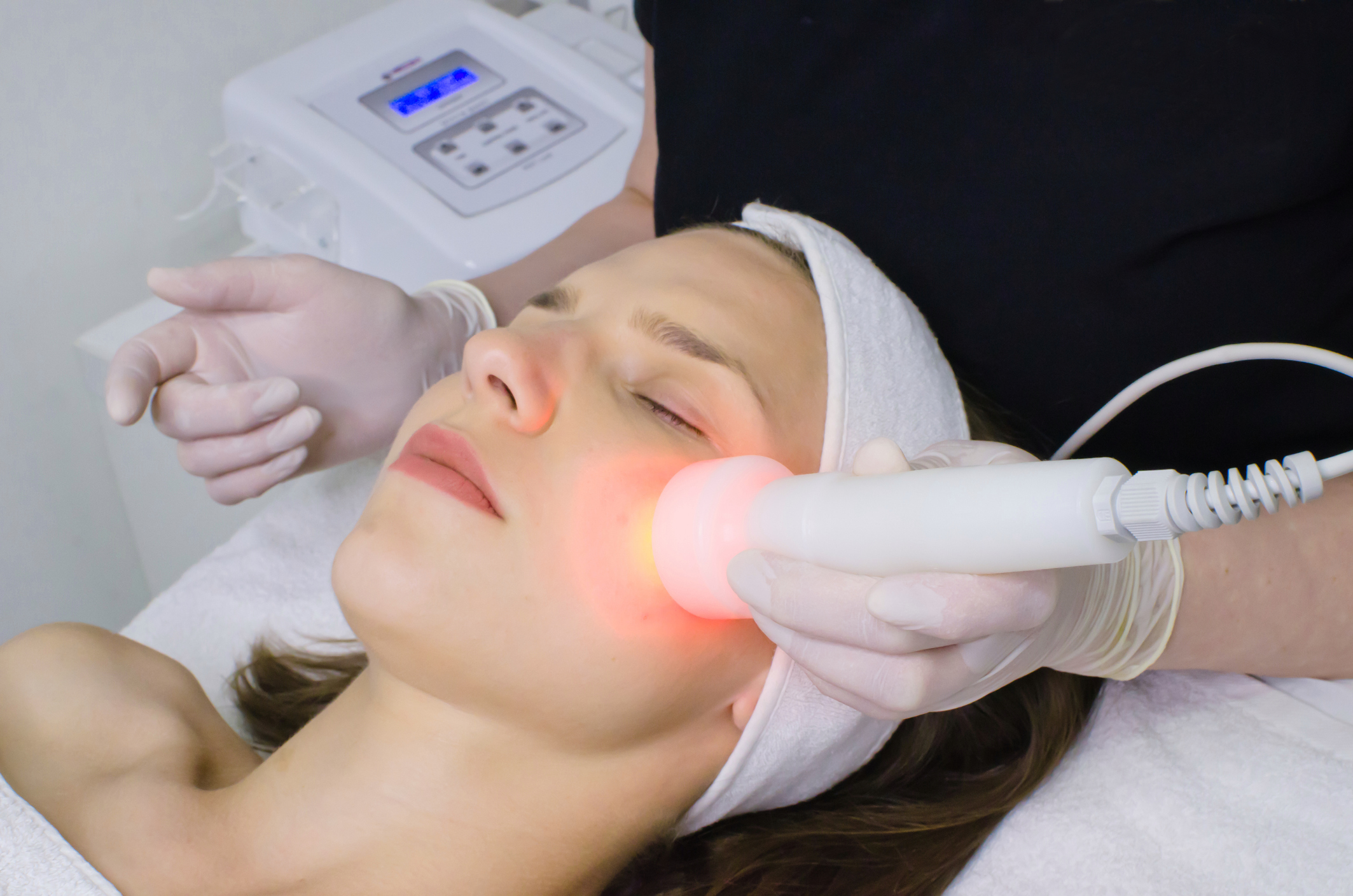 beautician doing red led light therapy to female customer in beauty salon, facial photo therapy for skin pore cleansing. Anti-aging treatments and photo rejuvenation procedure